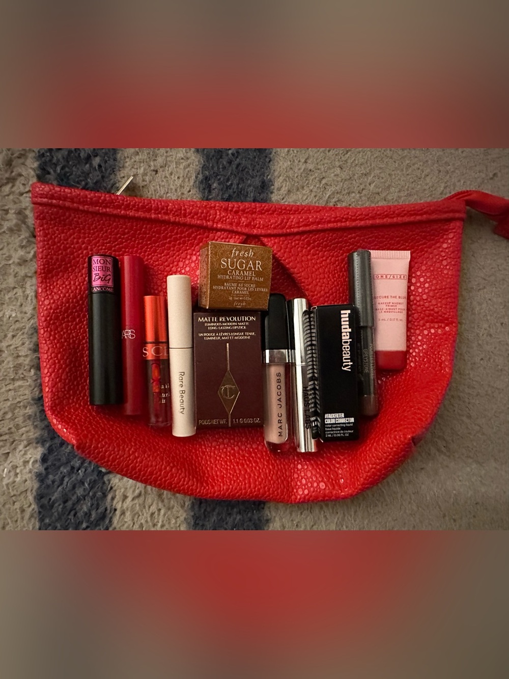 Assorted lip glosses, lipsticks and mascaras in a red Sephora cosmetic bag.